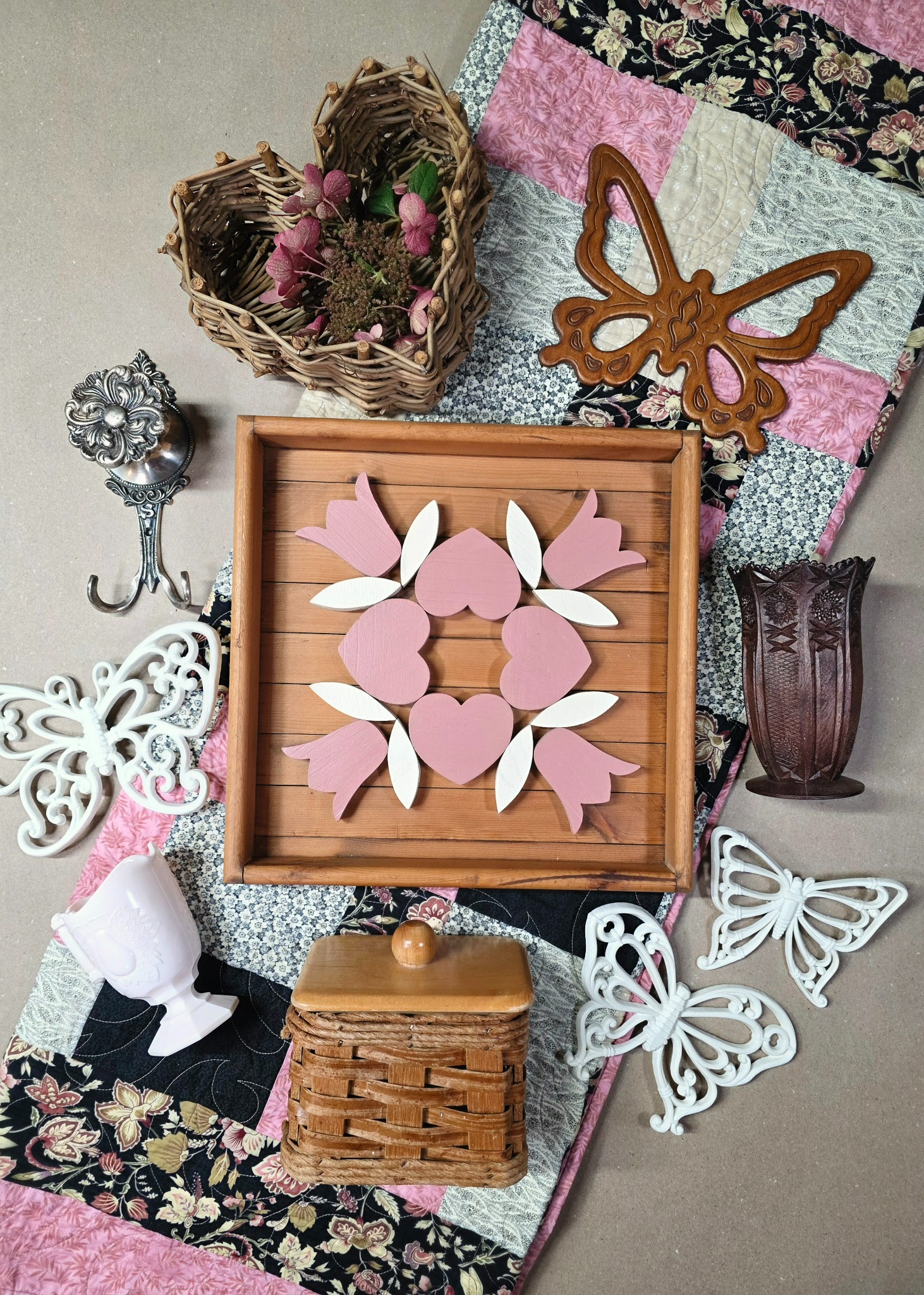 Patchwork Garden flat lay with pink heart folk art, butterfly décor, woven baskets, flowers, and a patchwork quilt