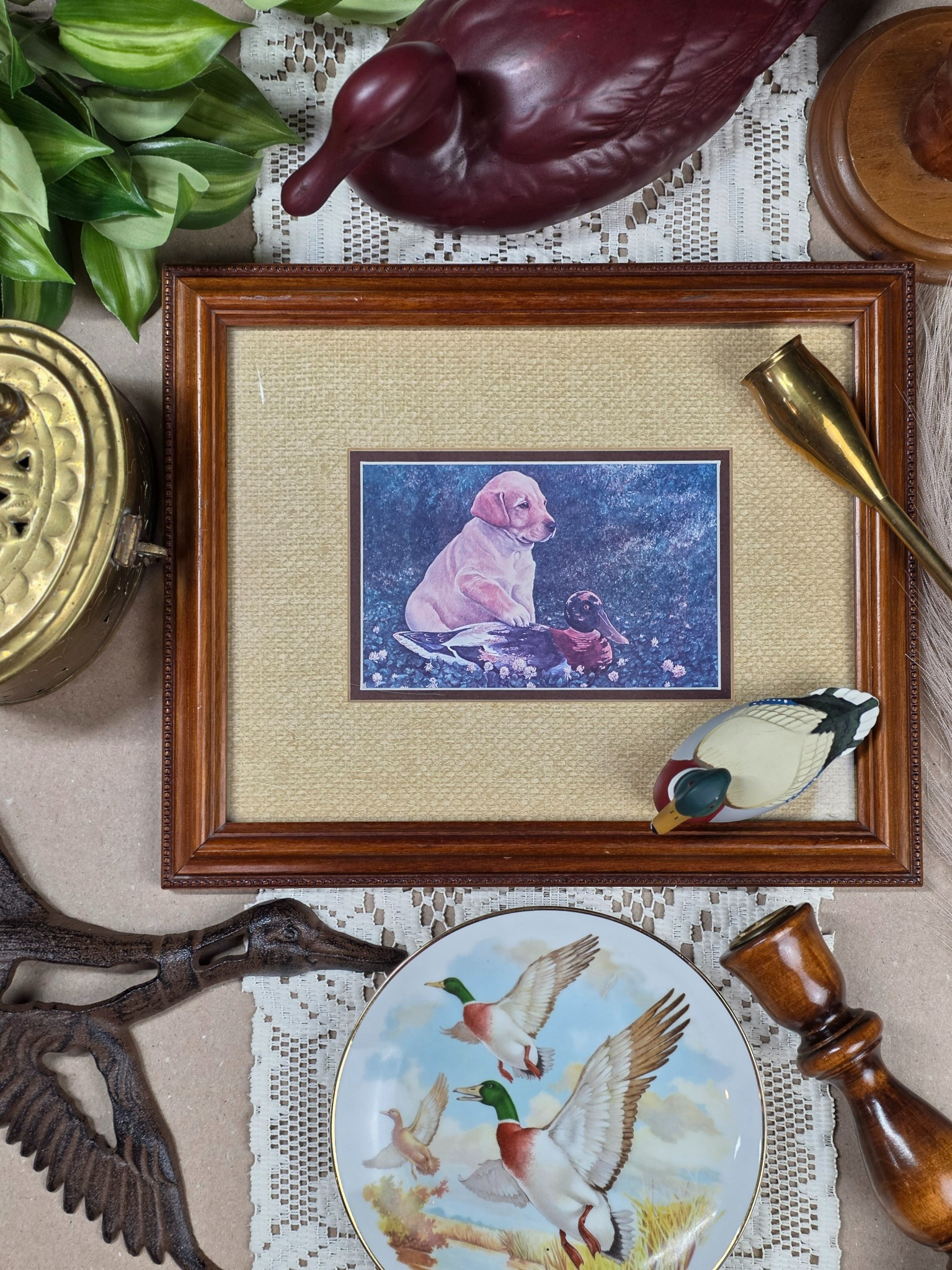 Pondside Puppy flat lay with framed puppy and duck artwork, mallard figurine, cast iron flying ducks, duck plate, brass accents, and lace
